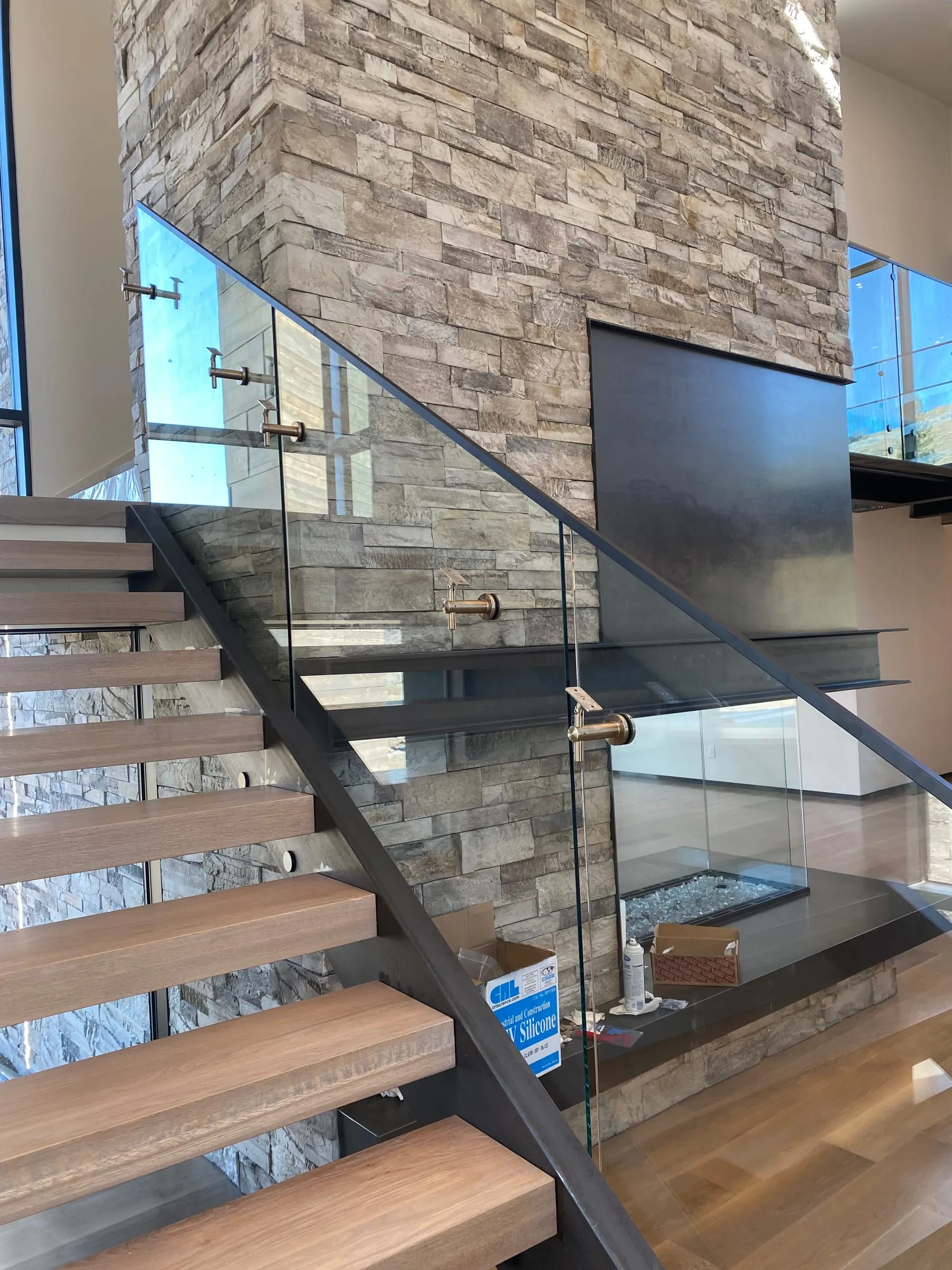 Glass railing with standoff hardware on a floating staircase beside a stacked stone wall